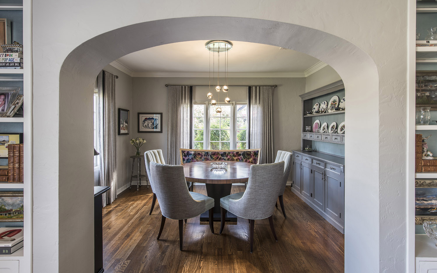 A dining room with arched doorway, modern lighting, built in cabinet with plates, and wood flooring in a historic home